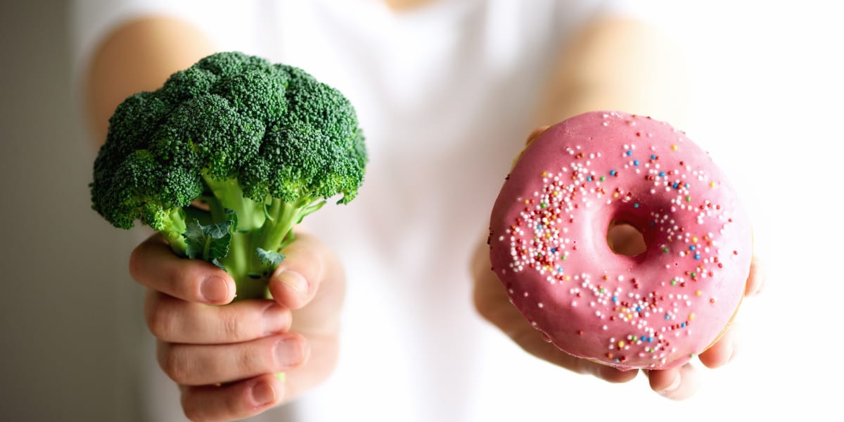 person holding a broccoli and a donut to illustrate healthy food choices